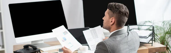 Trader holding infographics while looking at monitors with blank screen, banner — Stock Photo