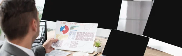 Back view of trader holding flipcharts near monitors with blank screen, blurred foreground, banner — Stock Photo