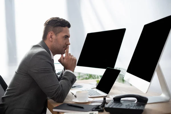 Side view of trader sitting at workplace near laptop and monitors with blank screen, blurred foreground — Stock Photo