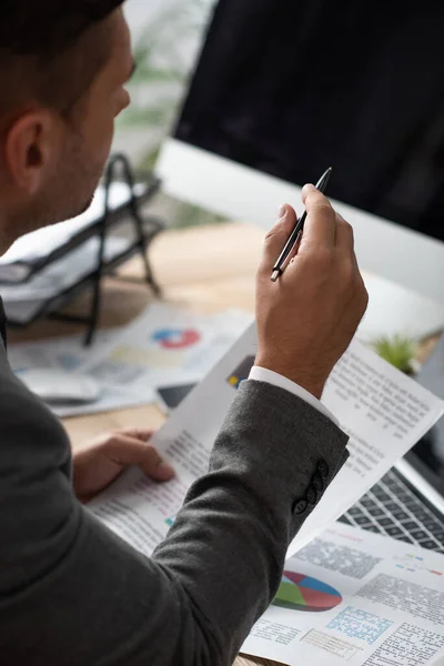 Vista ritagliata del commerciante che tiene infografica e punta con penna, primo piano sfocato — Foto stock