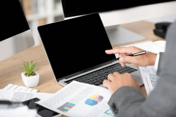 Vista recortada del comerciante apuntando con el dedo a la computadora portátil con pantalla en blanco, primer plano borrosa - foto de stock