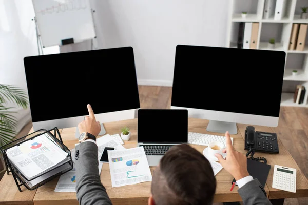 Vista aérea del comerciante apuntando con los dedos a los monitores con pantalla en blanco - foto de stock