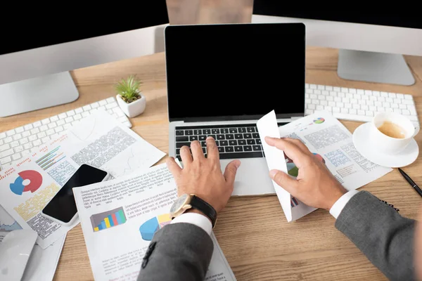 Cropped view of trader typing on laptop near papers with infographics — Stock Photo
