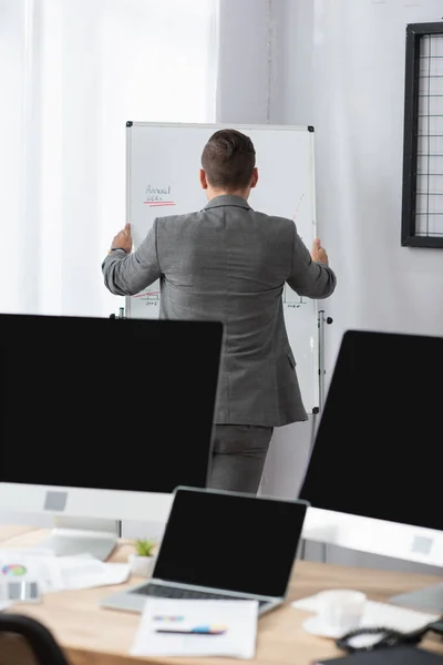 Back view of trader standing near flipchart and monitors with blank screen on blurred foreground — Stock Photo