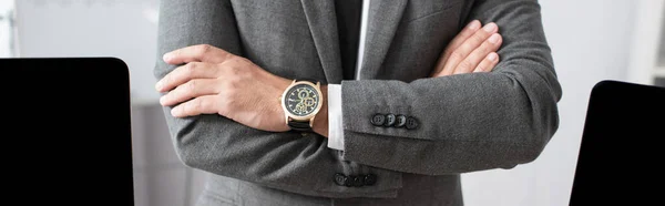 Vista parcial del comerciante en desgaste formal y reloj de pulsera de pie con brazos cruzados, bandera - foto de stock