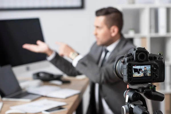 Selective focus of digital camera near businessman pointing with hands at computer monitors during online streaming on blurred background — Stock Photo