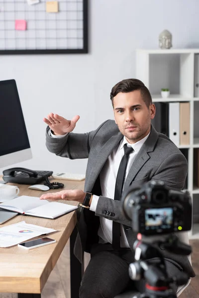 Händler zeigt Menge Geste beim Videostreaming auf Digitalkamera, verschwommener Vordergrund — Stockfoto