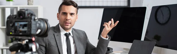 Businessman pointing with hand at computer monitors near digital camera on blurred background, banner — Stock Photo