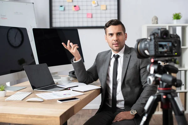 Financial trader pointing with hand at computer monitors in front of digital camera on blurred foreground — Stock Photo