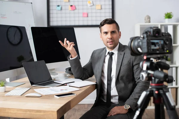 Comerciante financiero apuntando con la mano a los monitores de ordenador delante de la cámara digital en primer plano borrosa - foto de stock