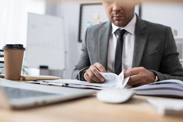 Ausgeschnittene Ansicht eines Händlers, der mit Dokumenten in der Nähe von Coffee to go arbeitet, verschwommener Vordergrund — Stockfoto