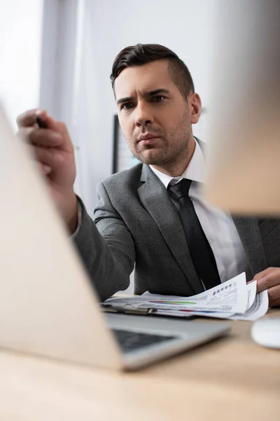 Uomo d'affari che punta al computer portatile in primo piano sfocato — Foto stock