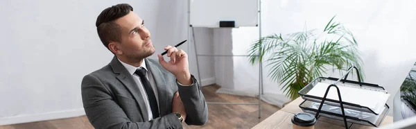 Nachdenklicher Händler, der Stift in der Hand hält und am Arbeitsplatz im Büro wegsieht, Banner — Stockfoto