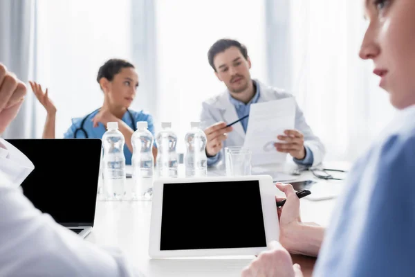 Enfermera sosteniendo tableta digital con pantalla en blanco cerca del médico en primer plano borroso en la clínica - foto de stock