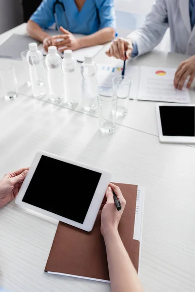 Cropped view of nurse holding digital tablet with blank screen near paper folder and colleagues on blurred background — Stock Photo