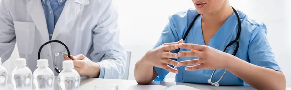 Ausgeschnittene Ansicht einer afrikanisch-amerikanischen Krankenschwester, die mit Stethoskop und Wasserflaschen in der Nähe des Arztes sitzt, Banner — Stockfoto