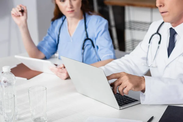 Ausgeschnittene Ansicht des Arztes zeigt auf Laptop in der Nähe der Krankenschwester mit digitalem Tablet auf verschwommenem Hintergrund — Stockfoto