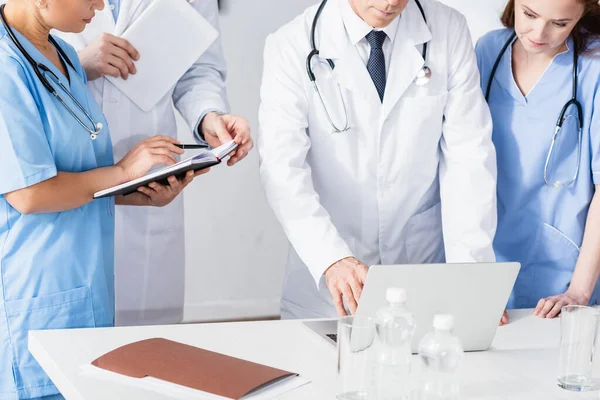 Doctors and nurses with notebook and devices working near paper folder and water on blurred foreground in clinic — Stock Photo