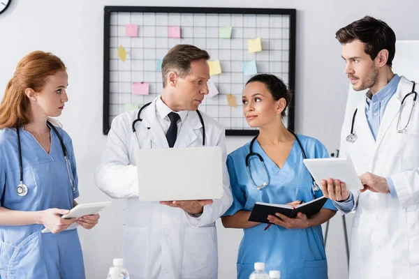 Personal hospitalario multicultural con dispositivos y cuaderno de trabajo en la clínica — Stock Photo