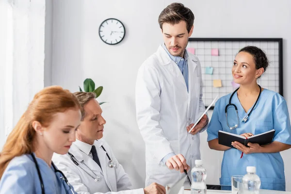 Multiethnic hospital staff with notebook and digital tablet working together in hospital — Stock Photo