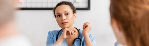 Enfermera afroamericana mirando a su colega en primer plano borroso, pancarta - foto de stock