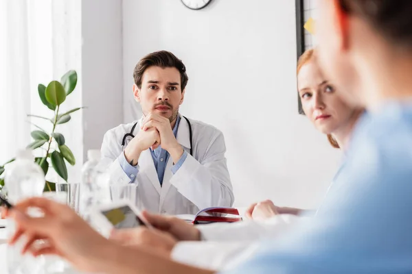 Doctor looking at colleague while working with notebook and digital tablet on blurred foreground — Stock Photo