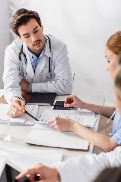 Médecin pointant vers les papiers près de tablette numérique et infirmière sur le premier plan flou — Photo de stock