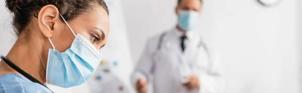 African american nurse in medical mask near doctor on blurred background in hospital, banner — Stock Photo