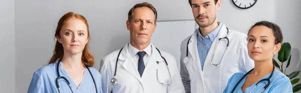 Multiethnic nurses and doctors with stethoscopes looking at camera in hospital, banner — Stock Photo