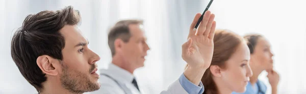 Médico con la mano levantada cerca de colegas multiculturales durante la reunión en el hospital sobre fondo borroso, pancarta - foto de stock