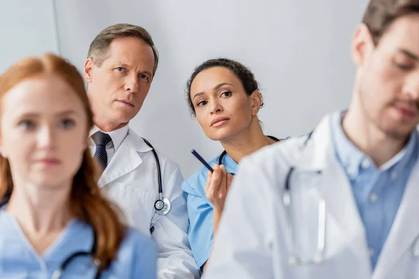 Concentrated multicultural colleagues looking away during meeting on blurred foreground in hospital — Stock Photo