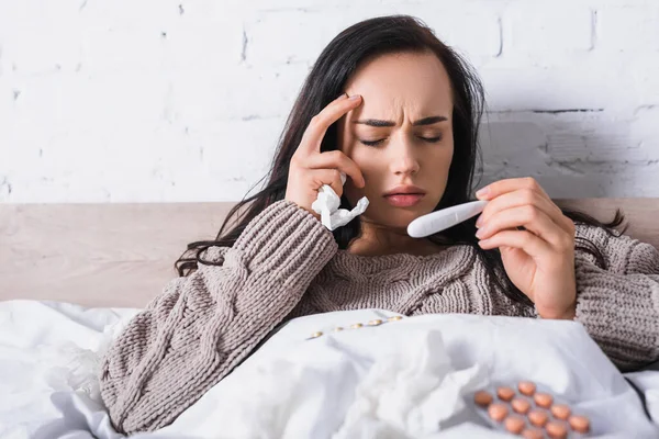 Sick young brunette woman with tissue and thermometer in bed — Stock Photo