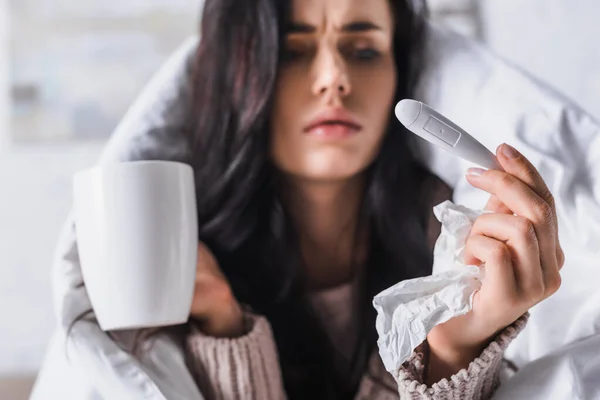 Malade jeune femme brune avec tissu, thermomètre et boisson chaude au lit — Photo de stock