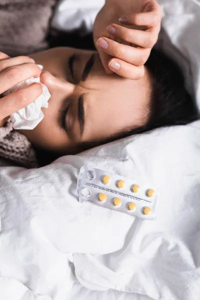 Malade jeune femme brune avec des pilules et le nez qui coule au lit — Photo de stock