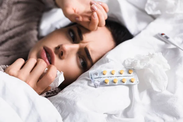 Enferma joven morena mujer con píldoras y tejido en la cama — Stock Photo