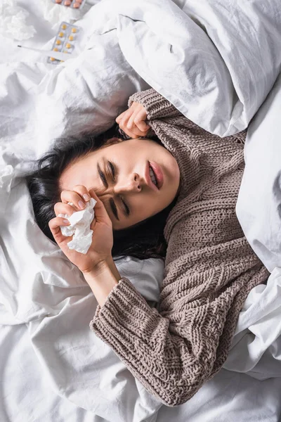 Top view of sick young brunette woman with pills and tissue in bed — Stock Photo