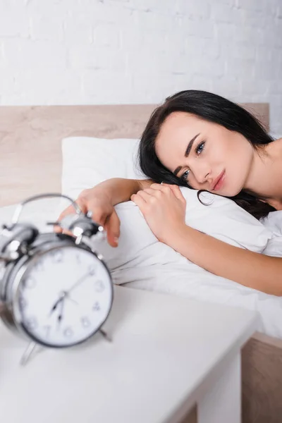 Reloj despertador clásico borrosa y joven morena en la cama en el fondo - foto de stock