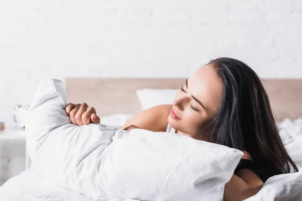 Joven morena mujer en la cama con almohada - foto de stock