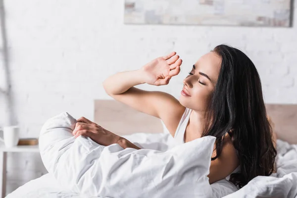 Jovem morena mulher na cama contra a luz solar — Fotografia de Stock