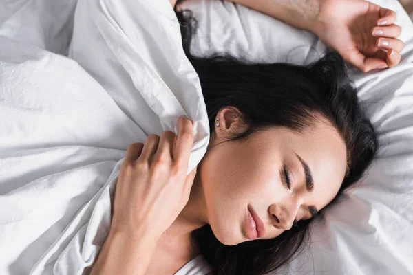 Top view of young brunette woman in bed sleeping under blanket — стоковое фото