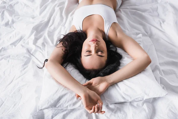 Top view of young brunette woman lying in bed with closed eyes — стоковое фото