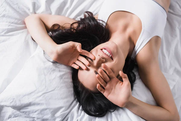 Vista superior da jovem mulher morena sorridente deitada na cama — Fotografia de Stock