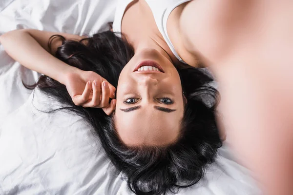 Top view of young smiling brunette woman lying in bed — стоковое фото