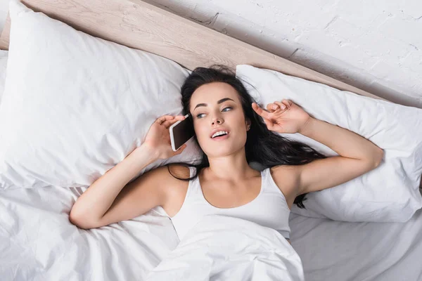 Молода брюнетка говорить на смартфоні в ліжку — стокове фото