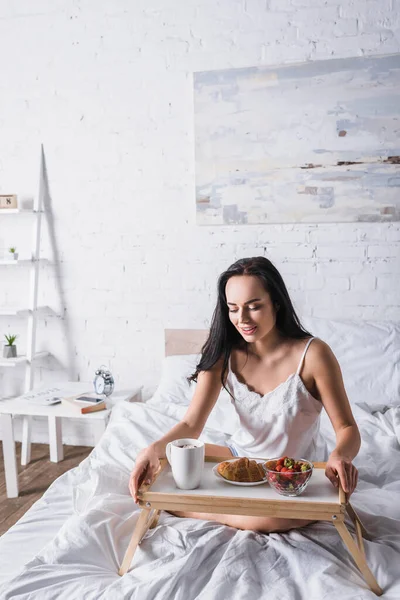 Молода брюнетка має круасан і полуницю на сніданок у ліжку — стокове фото