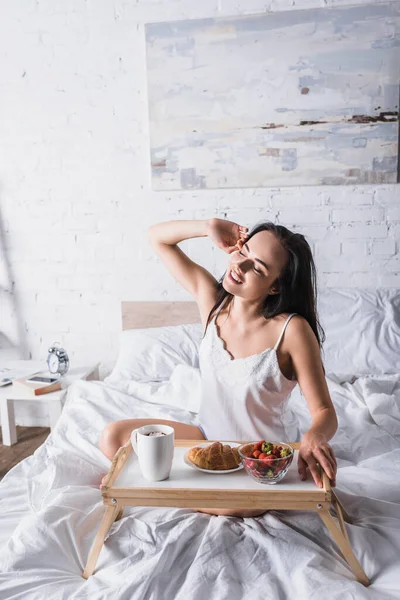 Junge brünette Frau mit Croissant und Erdbeere zum Frühstück im Bett — Stockfoto