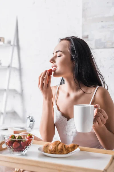 Junge brünette Frau isst Erdbeere zum Frühstück im Bett — Stockfoto