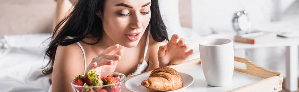 Junge brünette Frau mit Croissant, Erdbeere und Kakao zum Frühstück im Bett, Banner — Stockfoto