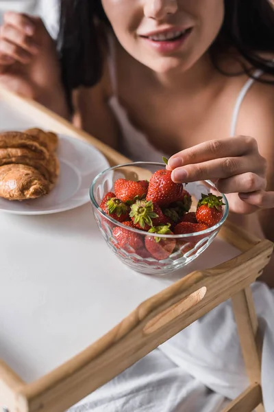 Abgeschnittene Ansicht einer Frau mit Croissant, Erdbeere zum Frühstück im Bett — Stockfoto