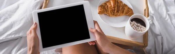 Vue recadrée de la femme ayant croissant et cacao pour le petit déjeuner tout en tenant tablette numérique au lit, bannière — Photo de stock